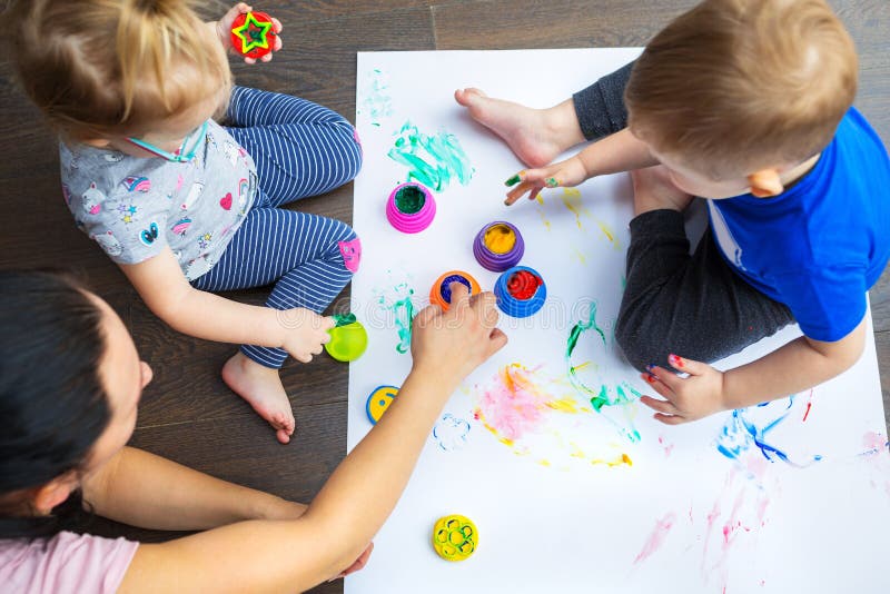 Happy family of mother and toddler twins are painting by hands