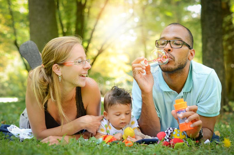 Šťastný interracial rodina je foukání bublin v parku.