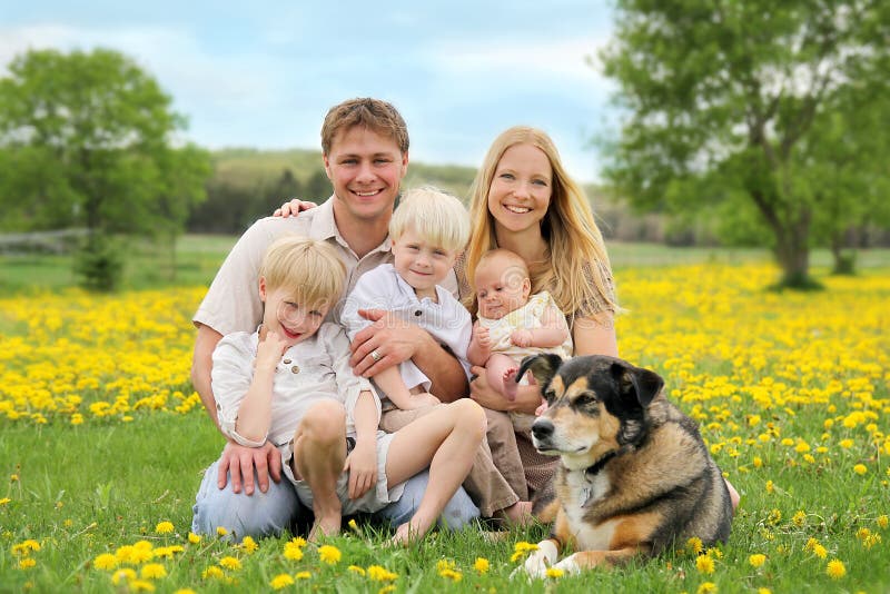 A portrait of a happy family of five caucasian people, including big brother, toddler boy, and baby sister are relaxing in a yellow Dandelion flower meadow with their pet dog. A portrait of a happy family of five caucasian people, including big brother, toddler boy, and baby sister are relaxing in a yellow Dandelion flower meadow with their pet dog.