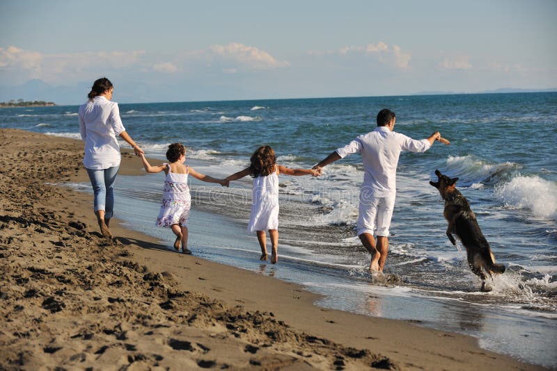 Šťastná mladá rodina v bílé oblečení bavit a hrát si s krásného psa na dovolenou na krásné pláži.