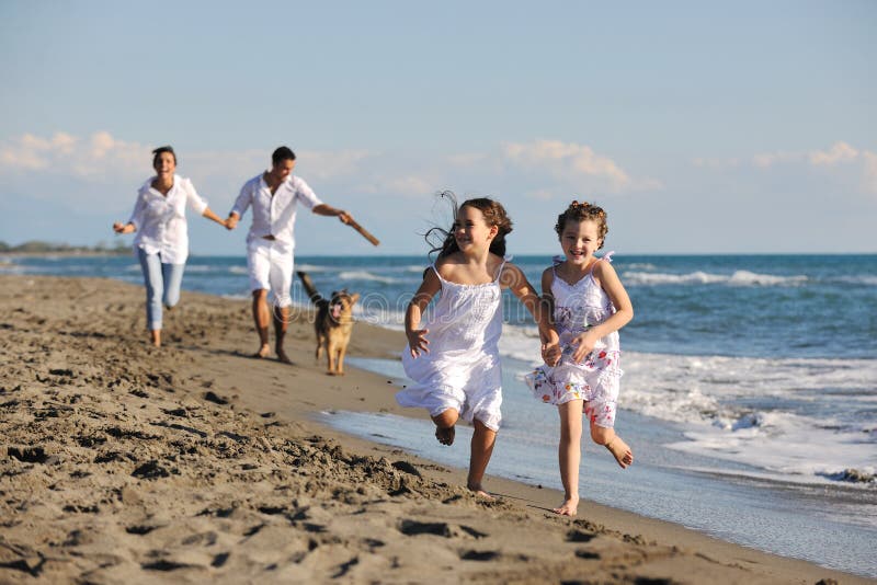 Giovani felici di famiglia in bianco abbigliamento divertirsi e giocare con un bel cane le vacanze sulla bellissima spiaggia.