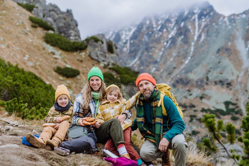 Šťastná rodina odpočívá, svačinu během společné turistiky v podzimních horách.