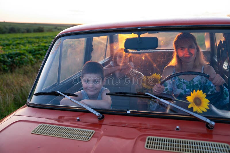 Happy family on a road trip in their car, young mother driving a red retro car with her teen children, enjoying stock photo Happy family on a road trip in their car, young mother driving a red retro car with her teen children, enjoying stock photo