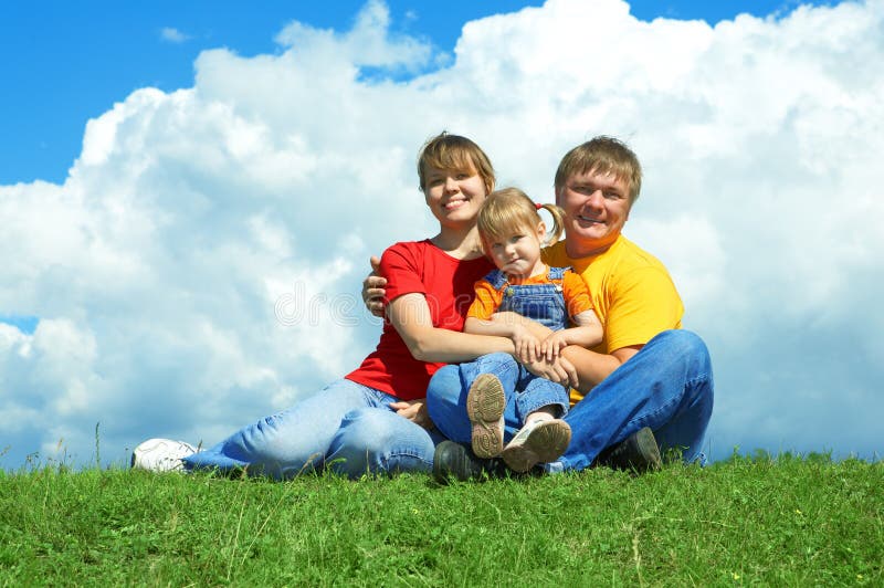 Happy family sit on green grass under sky