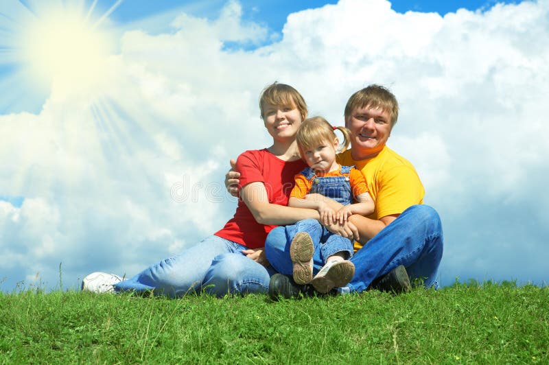 Happy family sit on green grass under sky