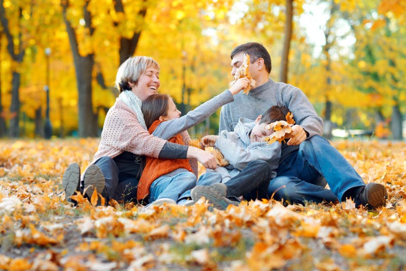 Happy family sitting on fallen leaves, playing and having fun in autumn city park. Children and parents together having a nice day royalty free stock images Happy family sitting on fallen leaves, playing and having fun in autumn city park. Children and parents together having a nice day royalty free stock images
