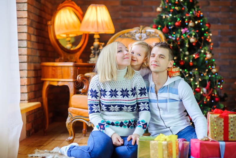 happy family sitting on the floor near the festive Christmas tree, daughter holding a small gift hugging parents, positive stock images happy family sitting on the floor near the festive Christmas tree, daughter holding a small gift hugging parents, positive stock images