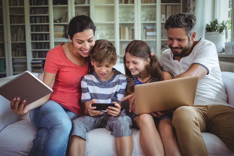 Happy family sitting on sofa and using laptop, mobile phone and digital tablet royalty free stock images