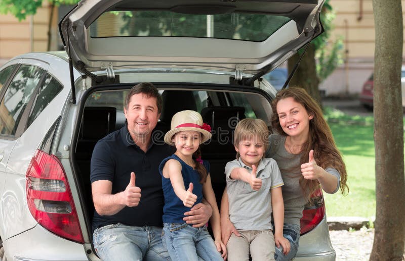 Happy family sitting in the trunk of a car and showing thumbs up