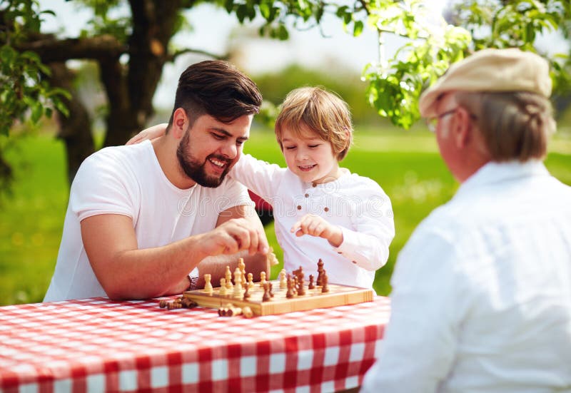Happy family of three generation of men playing chess in spring garden stock photography Happy family of three generation of men playing chess in spring garden stock photography