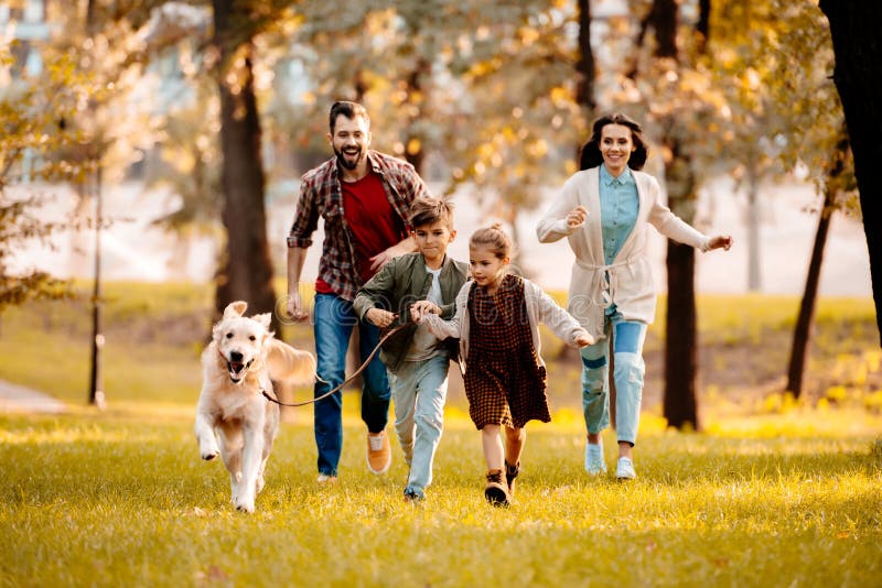 Happy family with two children running after a dog together in autumn park