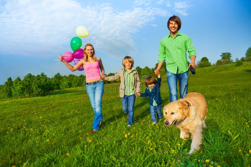 Happy family walks with balloons and dog in park in summer