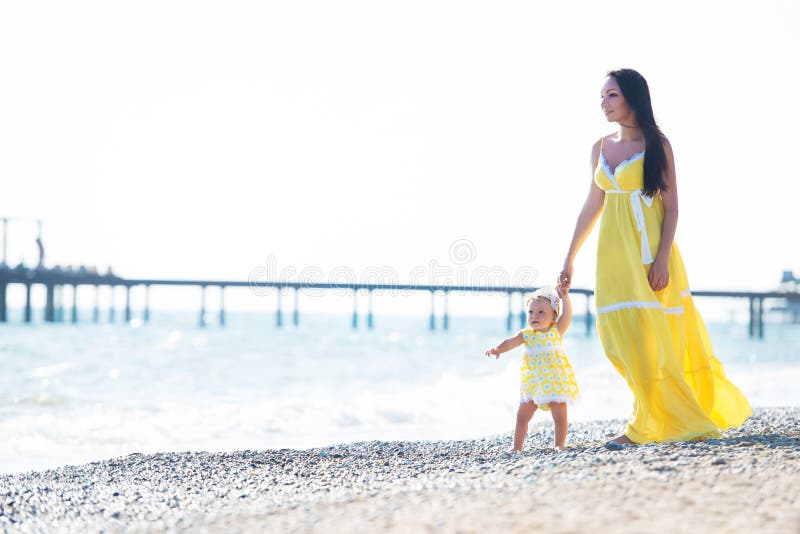 Happy family in a yellow dress. Mother and child are walking on the beach stock photo Happy family in a yellow dress. Mother and child are walking on the beach stock photo