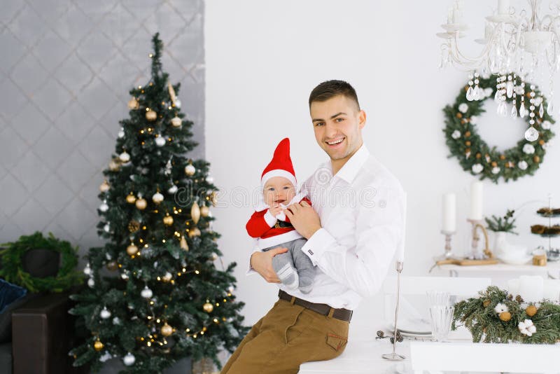 A happy father holds his young son in a Santa suit or hat in his arms in the living room near the Christmas tree. Happy New year royalty free stock photos A happy father holds his young son in a Santa suit or hat in his arms in the living room near the Christmas tree. Happy New year royalty free stock photos