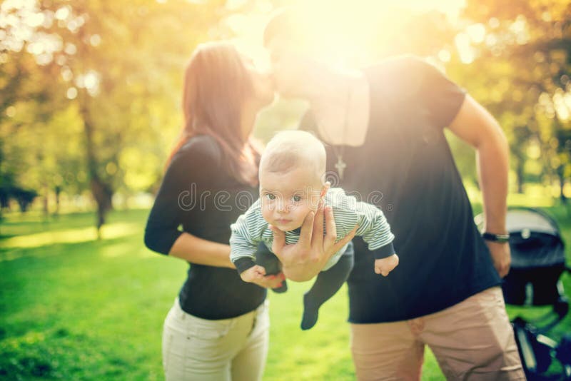 Happy father holds newborn baby on arm, kissing the mother of child. happy family in park, newborn kid and happiness