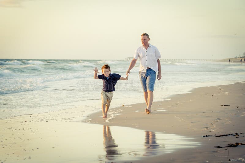 Happy father playing on the beach with little son running excited with barefoot in sand and water