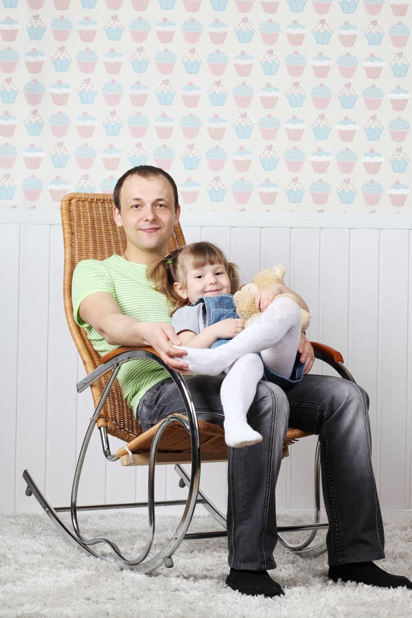 Happy father sits with little daughter in rocking chair