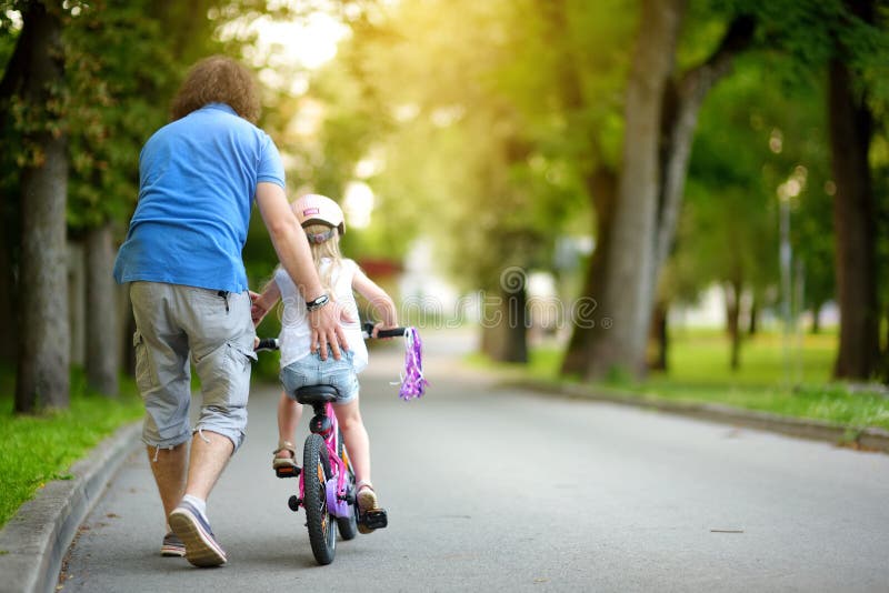 Happy father teaching his little daughter to ride a bicycle. Child learning to ride a bike. royalty free stock photos Happy father teaching his little daughter to ride a bicycle. Child learning to ride a bike. royalty free stock photos