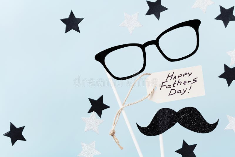 Happy Fathers Day background with greeting tag, glasses, funny moustache and star confetti on table top view. Flat lay composition.