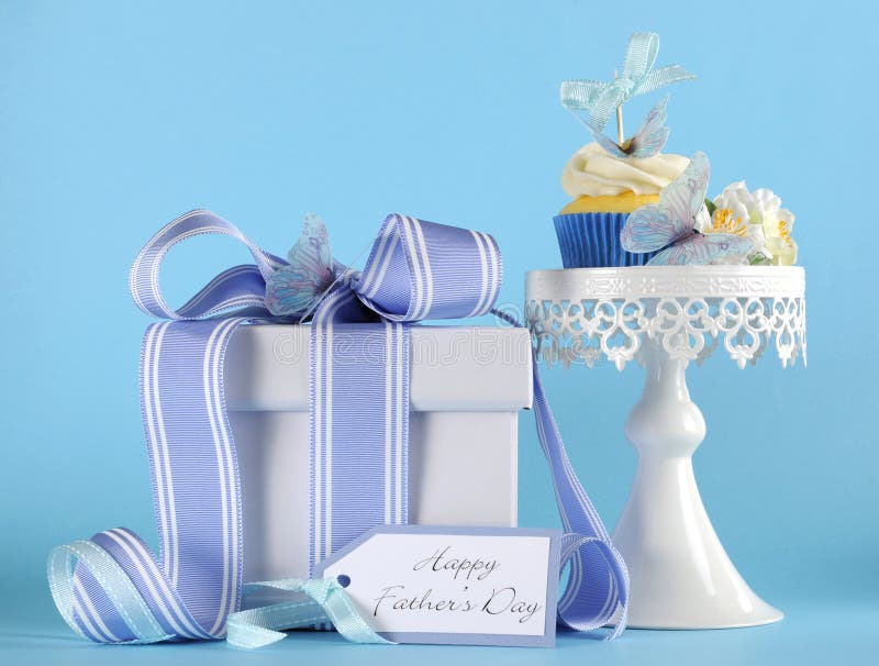 Happy Fathers Day blue butterfly theme cupcake on white cupcake stand with gift and greeting gift tag against a blue background.