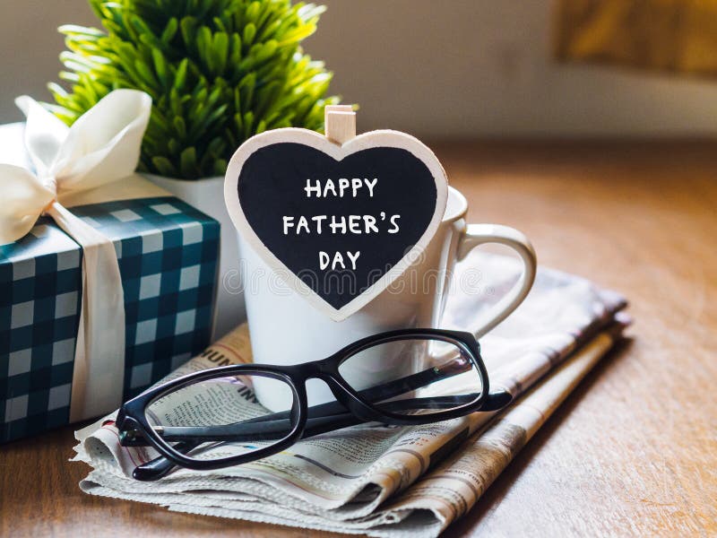 Happy fathers day concept. coffee cup with gift box, heart tag with Happy father`s day text and newspaper, glasses on wooden table background.
