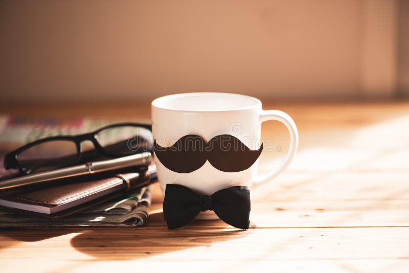 Happy fathers day concept. coffee cup with black paper mustache and newspaper, note book, glasses on wooden table background.