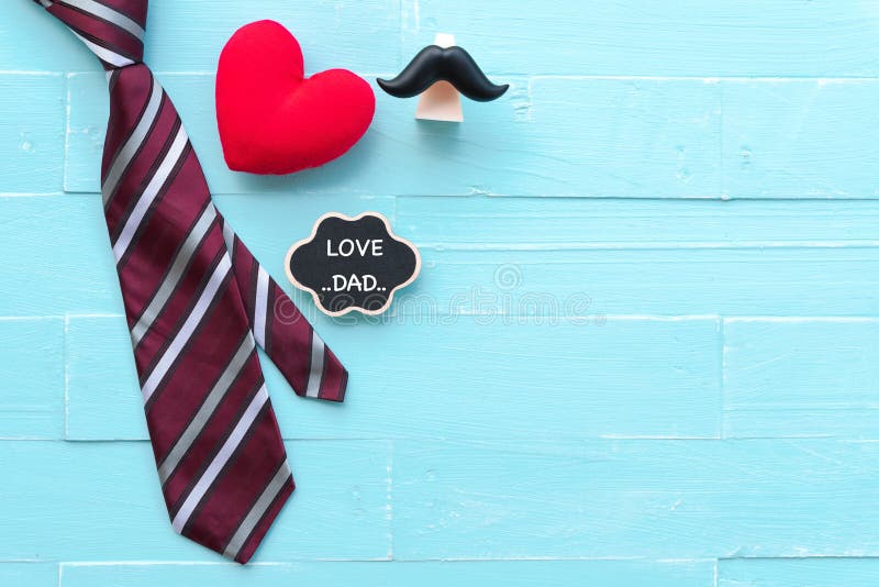Happy fathers day concept. Red tie, handmade red heart mustache with LOVE DAD text on bright blue pastel wooden table background.