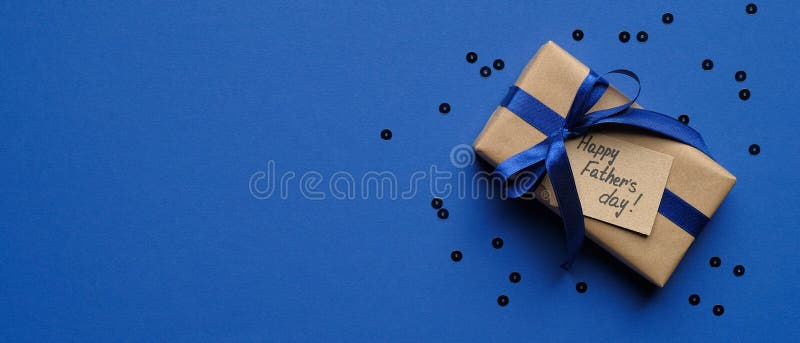 Happy Fathers Day concept. Wide banner mockup with gift box wrapped craft paper with blue ribbon and label Happy Father`s Day on blue background with confetti. Fathers Day sale promotion poster design