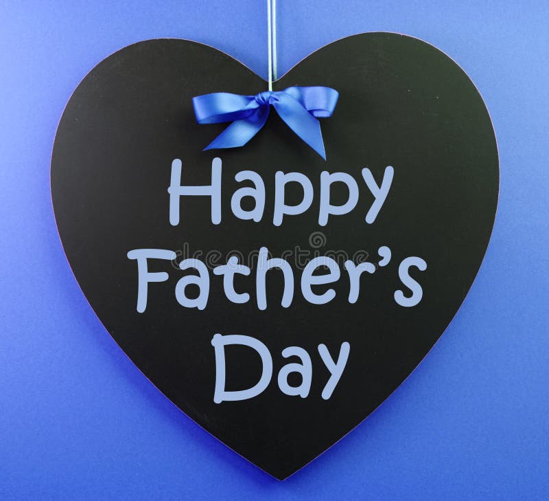 Happy Fathers Day message written on a heart shape black blackboard with blue ribbon against a blue background.