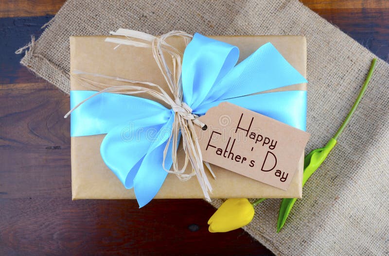 Happy Fathers Day natural kraft paper wrapped gift owith pale blue ribbon on dark wood background. Happy Fathers Day natural kraft paper wrapped gift owith pale blue ribbon on dark wood background.