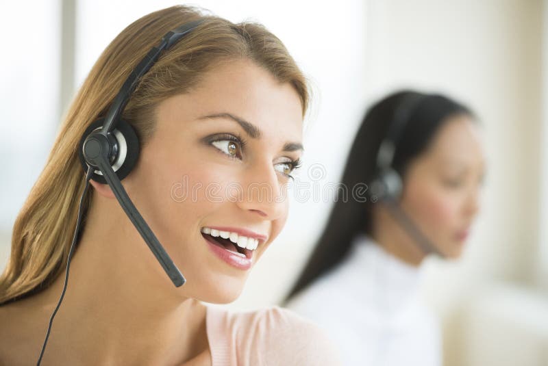 Close-up of happy female customer service representative looking away with colleague in background