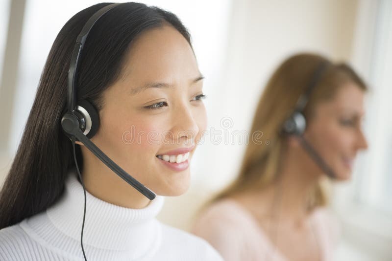 Happy female customer service representative wearing headset looking away with colleague in background. Happy female customer service representative wearing headset looking away with colleague in background