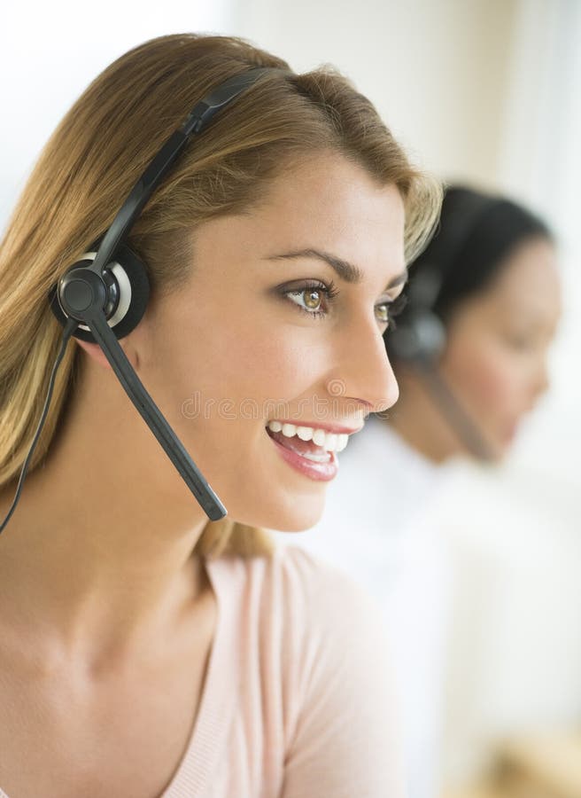 Close-up of happy female customer service representative wearing headset with colleague in background