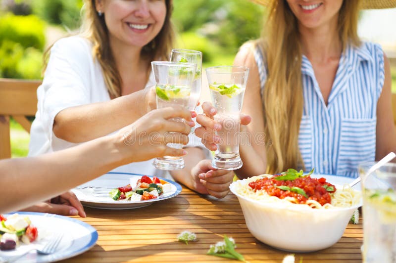 Happy female friends with glasses of lemonade at dining table in