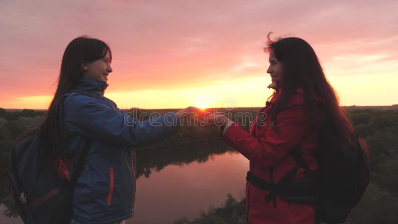 Happy female travelers stand high on the mountain and hold the sun in their hands at sunset in the sky. Women