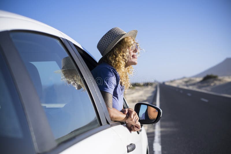 Happy freedom concept with beautiful lonely traveler adult caucasian woman enjoy the trip lifestyle outside the window of her white car - transport and long asphalt road in background