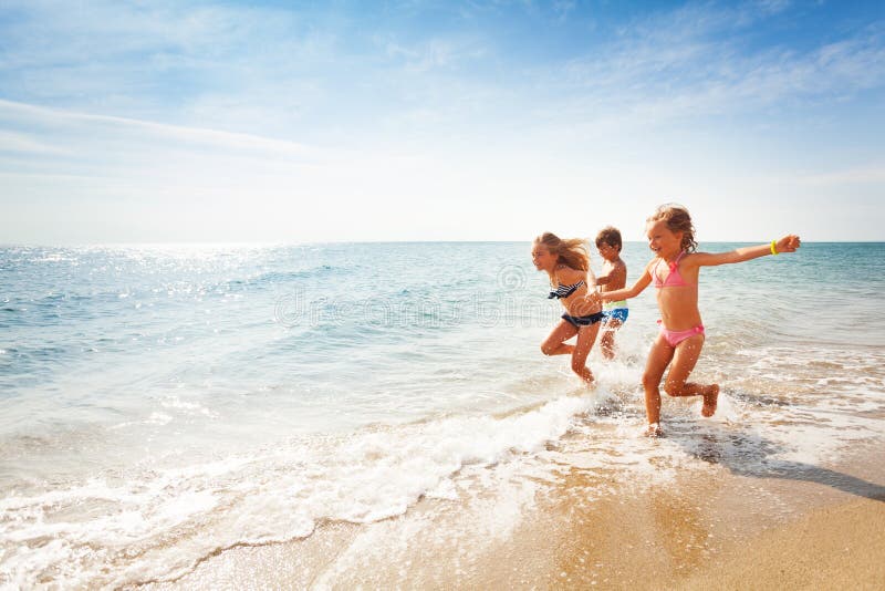 Happy friends running along edge of sea in summer