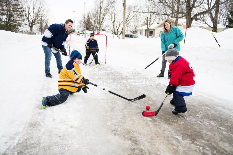 A Happy funny kids playing hockey with father on street in the winter season. A Happy funny kids playing hockey with father on street in the winter season