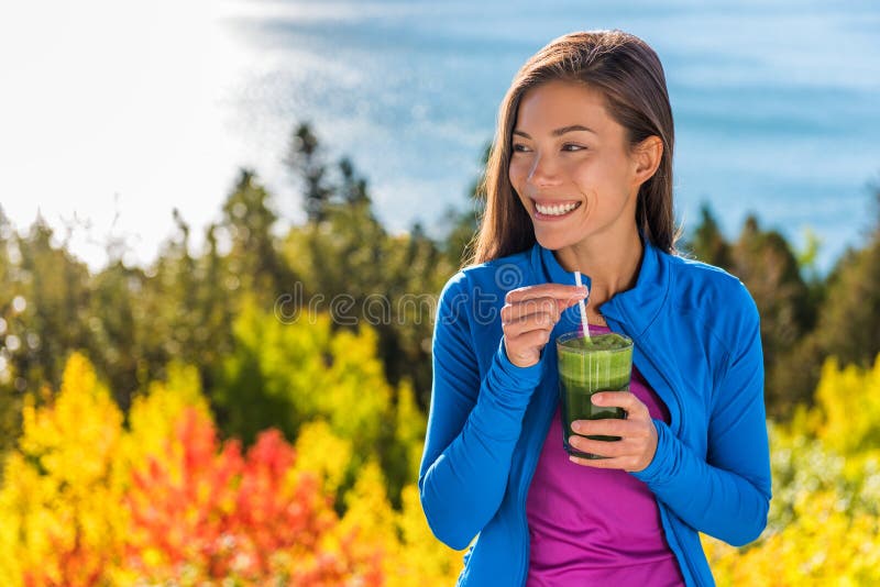 Happy healthy eating girl drinking green smoothie detox outdoors in fall autumn foliage nature retreat. Woman on weight loss diet vegan nutrition cleanse. Happy healthy eating girl drinking green smoothie detox outdoors in fall autumn foliage nature retreat. Woman on weight loss diet vegan nutrition cleanse