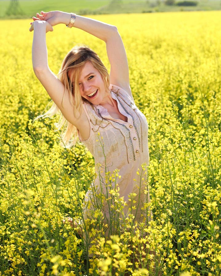 Happy girl with arms up, relaxing in the spring yellow field