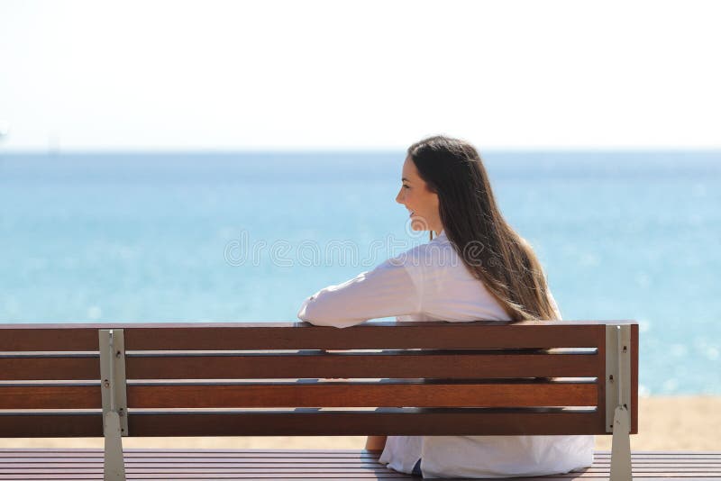 Happy girl on a bench contemplating ocean on the beach