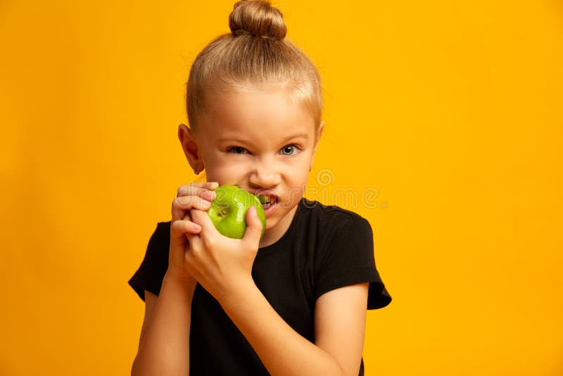 Happy girl eating green apple, closeup pretty girl bits fresh apple isolated on a yellow background