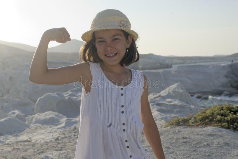 Half body portrait of happy young girl in dress and hat flexing bicep muscle, rocky landscape in background. Half body portrait of happy young girl in dress and hat flexing bicep muscle, rocky landscape in background.