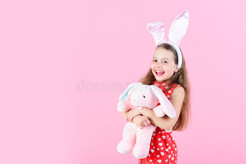 Happy girl holding rabbit toy on pink background