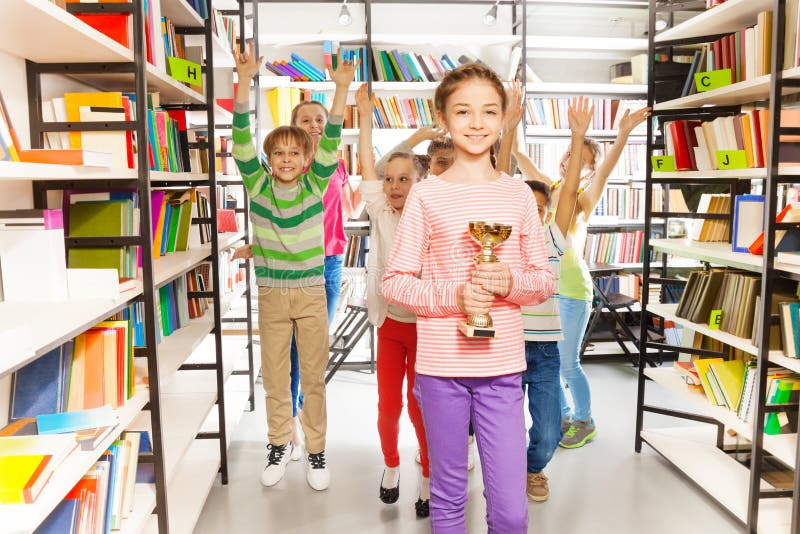 Happy girl holds golden cup, kids jumping behind royalty free stock photography Happy girl holds golden cup, kids jumping behind royalty free stock photography
