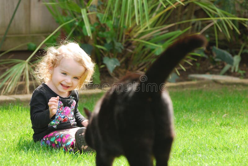 Happy girl laughs as cat walks towards her