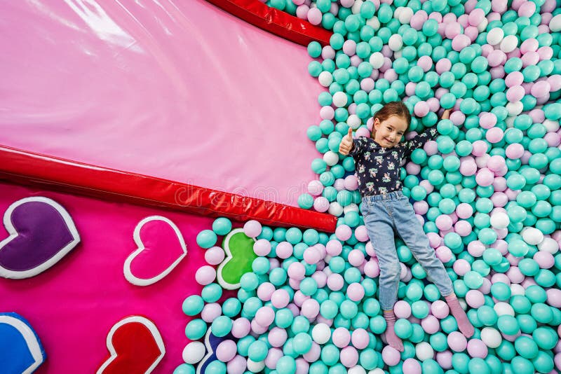 Happy girl playing at indoor play center playground. Lying at color balls in ball pool