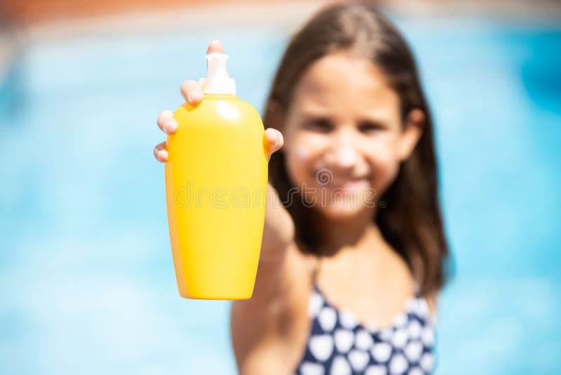 Happy girl in the pool showing a bottle of sunscreen