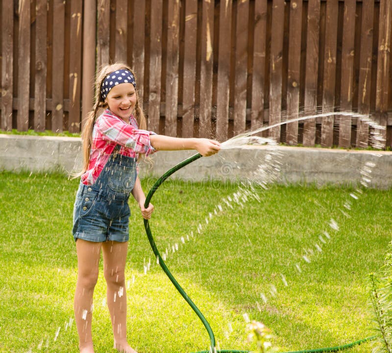 Happy girl pours water from a hose.