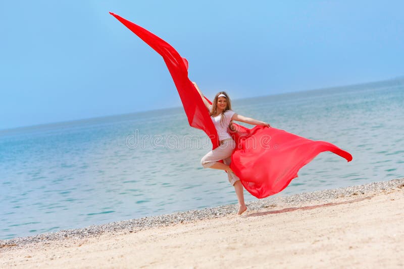 Happy girl with red wings jumping on beach